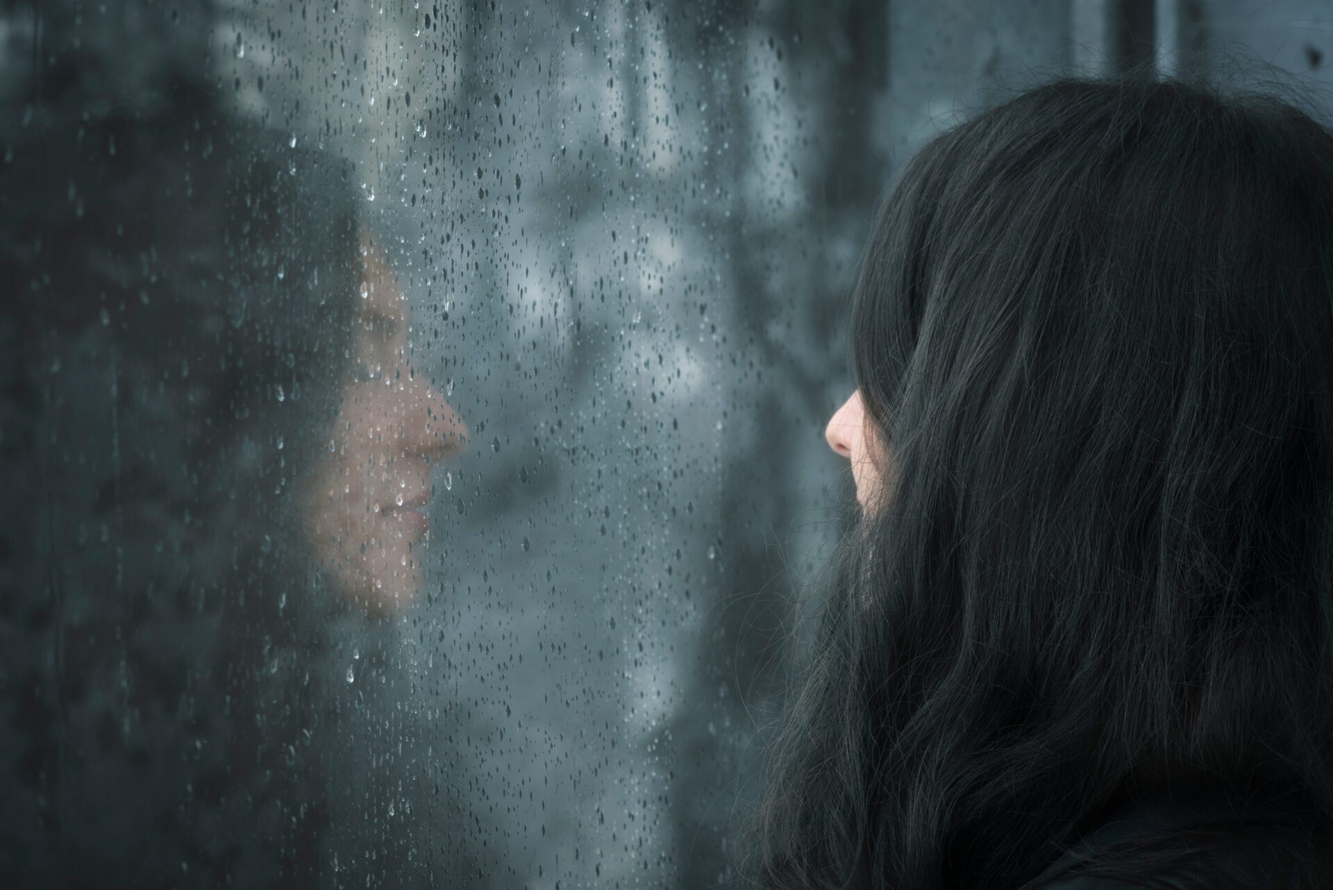 Woman in front of rainy window Profile image of a young brunette woman with closed eyes thinking in front of rainy window